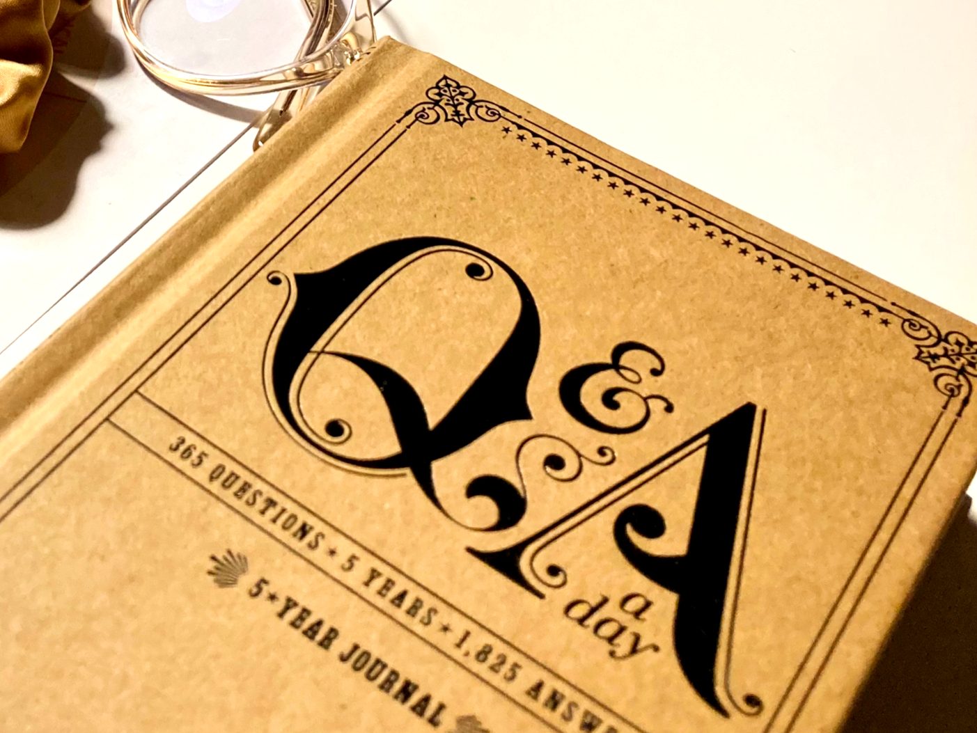 A journal, glasses and a hairband are placed on a white table.