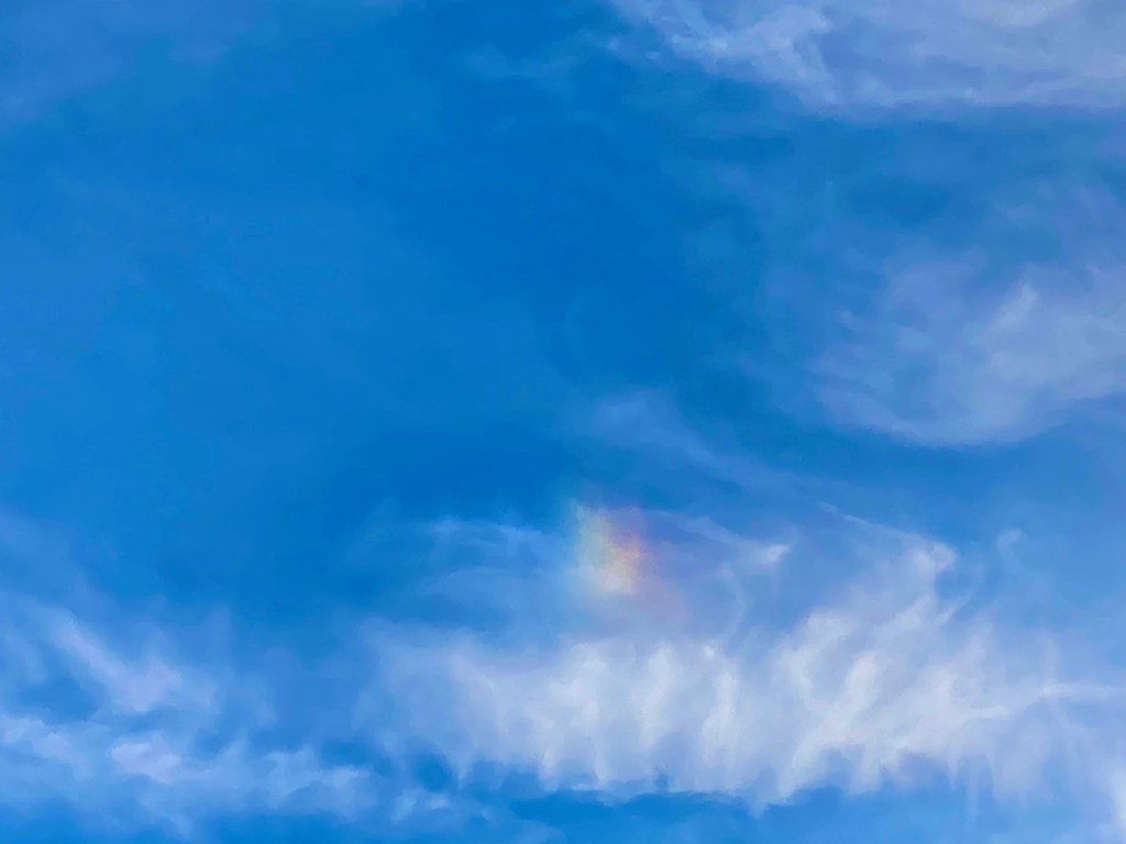 Blue sky with white wispy clouds and a small rainbow-like cloud.